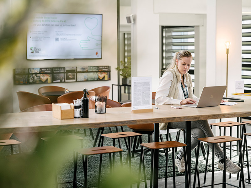 Moderne fælles lounge og kontorområde med kvinde der arbejder på bærbar i DTU Science Park.